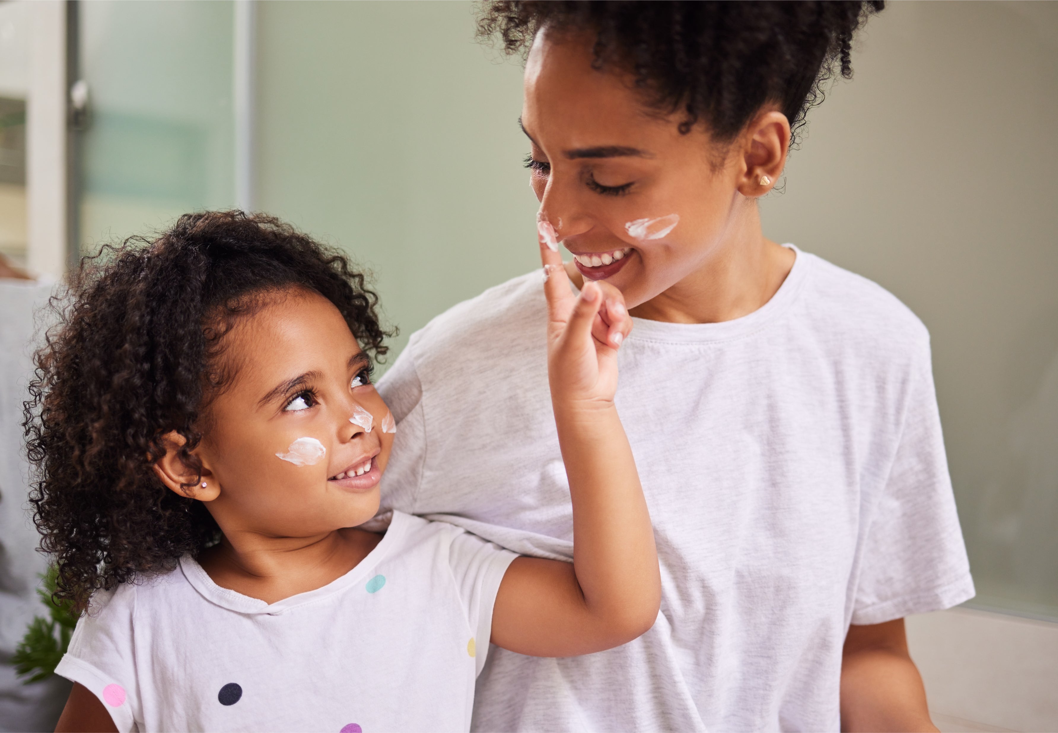 A parent gently applying cream to a school-age child's arm in a bright, naturally lit home setting.
