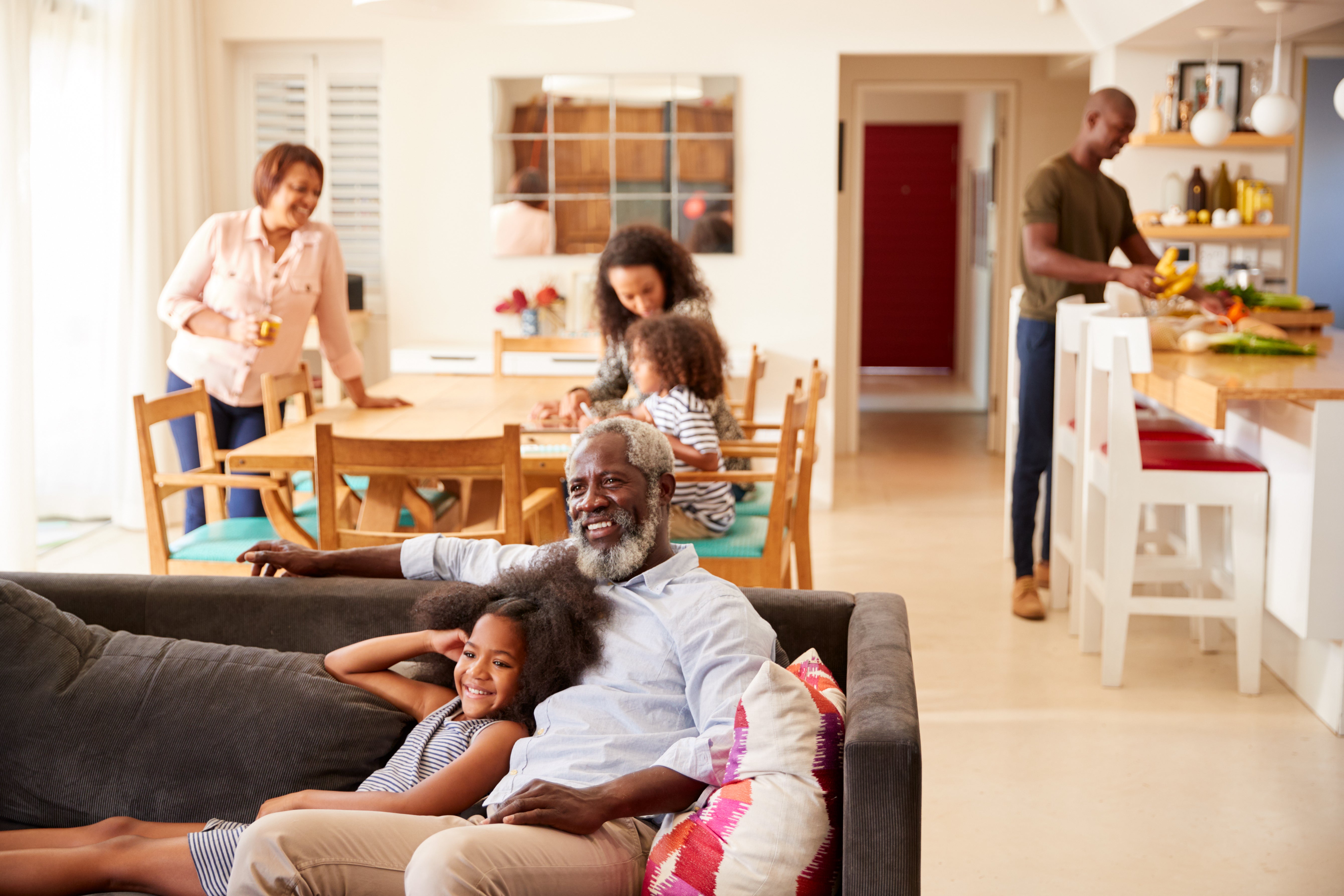Multigenerational Black family relaxing together at home, grandfather and granddaughter on sofa in foreground